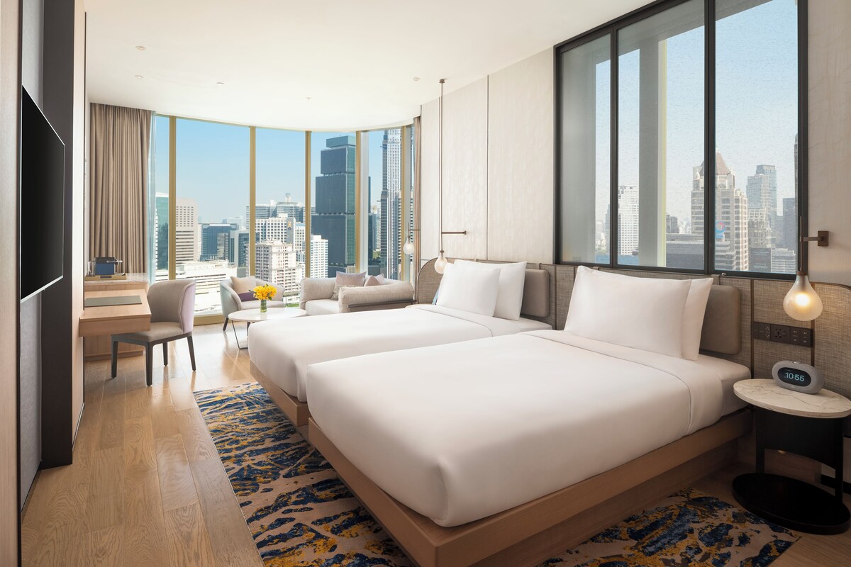 Une chambre d’hôtel avec deux lits, un bureau, une chaise, une télévision et une vue sur le panorama de la ville.