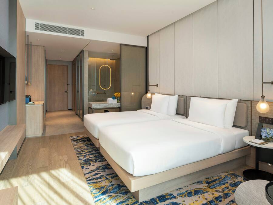 Una habitación de hotel moderna con una cama grande, mesitas de noche, un televisor y un baño visible a través de una puerta abierta.