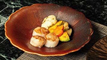 A ceramic bowl with scallops and vegetables on a textured mat.