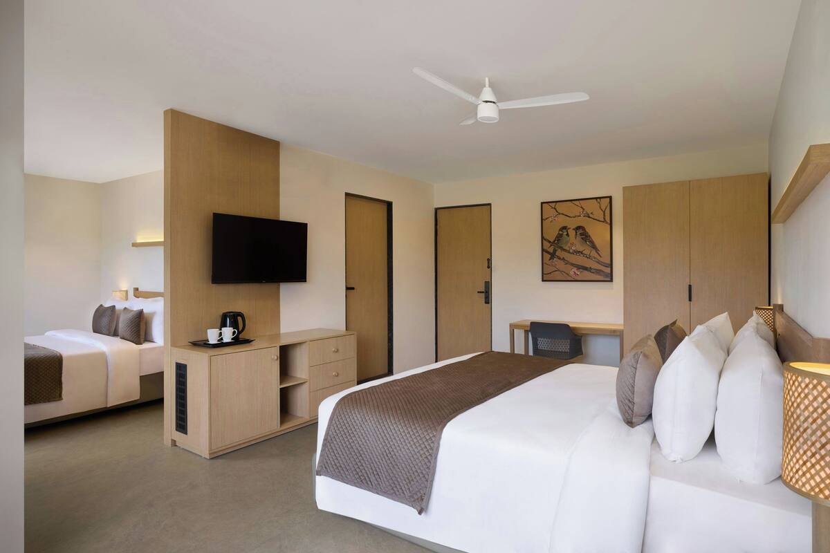 A hotel room with a large bed, a desk, a television, and a ceiling fan.