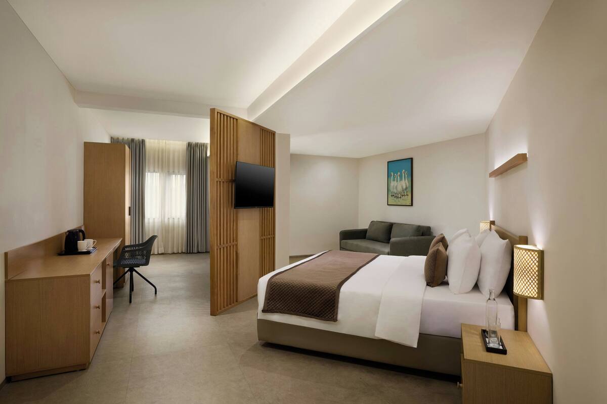 A hotel room with a bed, a desk, a chair, a TV, a sofa, and a lamp.