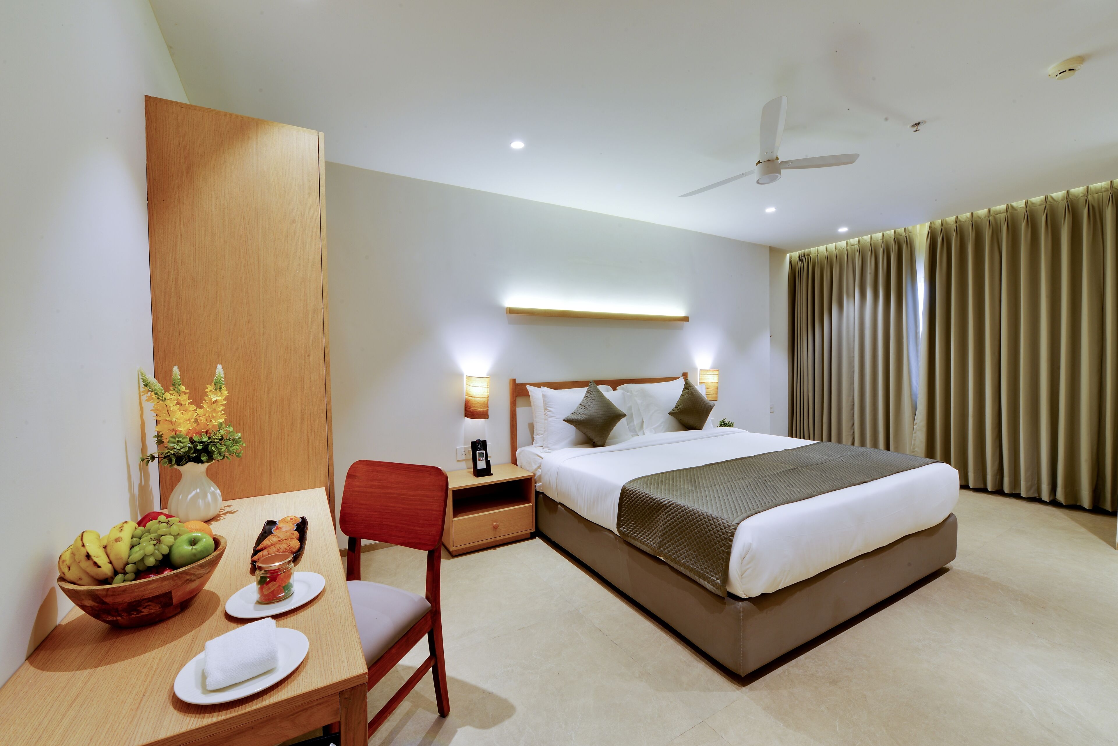 Une chambre d’hôtel comprenant un lit, une table de chevet, une chaise et un bureau avec un panier de fruits et un vase de fleurs.