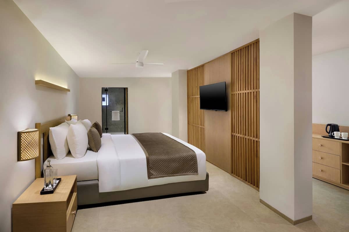 A modern hotel room with a bed, bedside table, TV, wardrobe, and a coffee maker.
