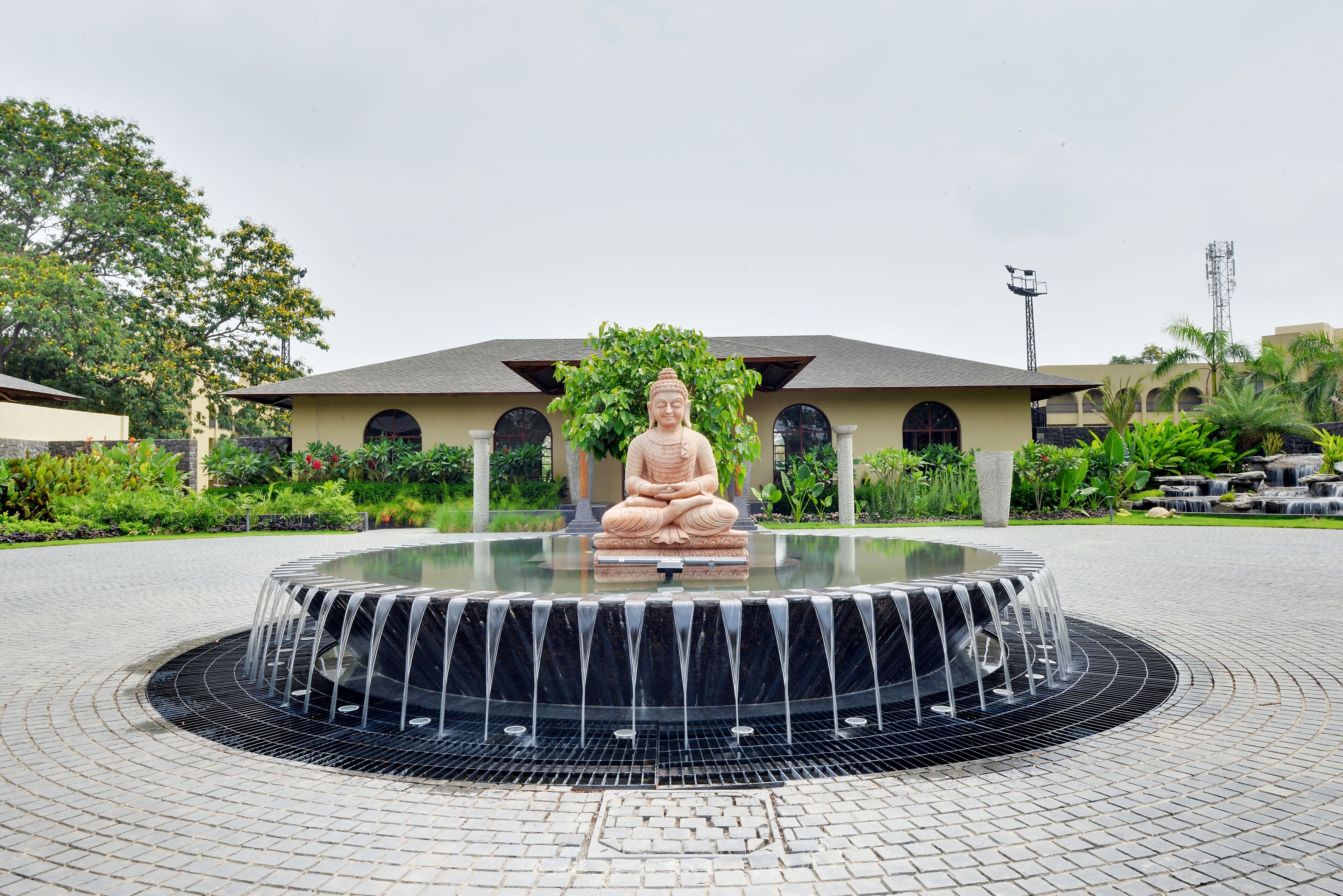 A Buddha statue in a circular water feature with a paved walkway and greenery in the background.