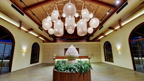 Un hall espacioso con un amplio banco de madera, una planta ornamental en el centro y un techo con múltiples lámparas colgantes.