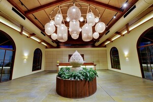 A spacious lobby with a large wooden bench, a central decorative planter, and a ceiling with multiple hanging light fixtures.