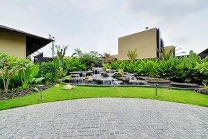 A landscaped area with a paved walkway, a small waterfall feature, and lush greenery.