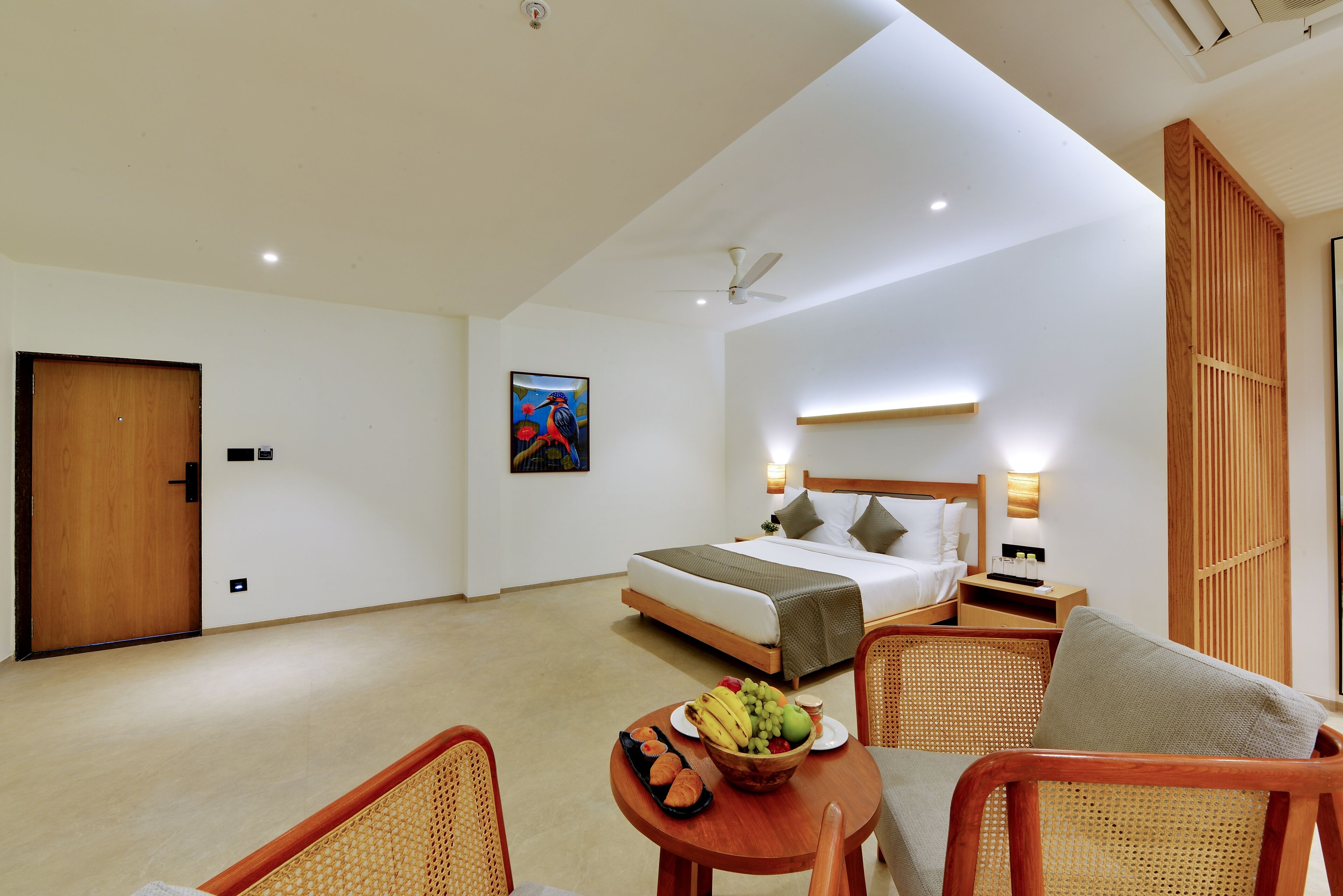 Una habitación de hotel con cama, mesita de noche, silla y una mesa con fruta y bollería.