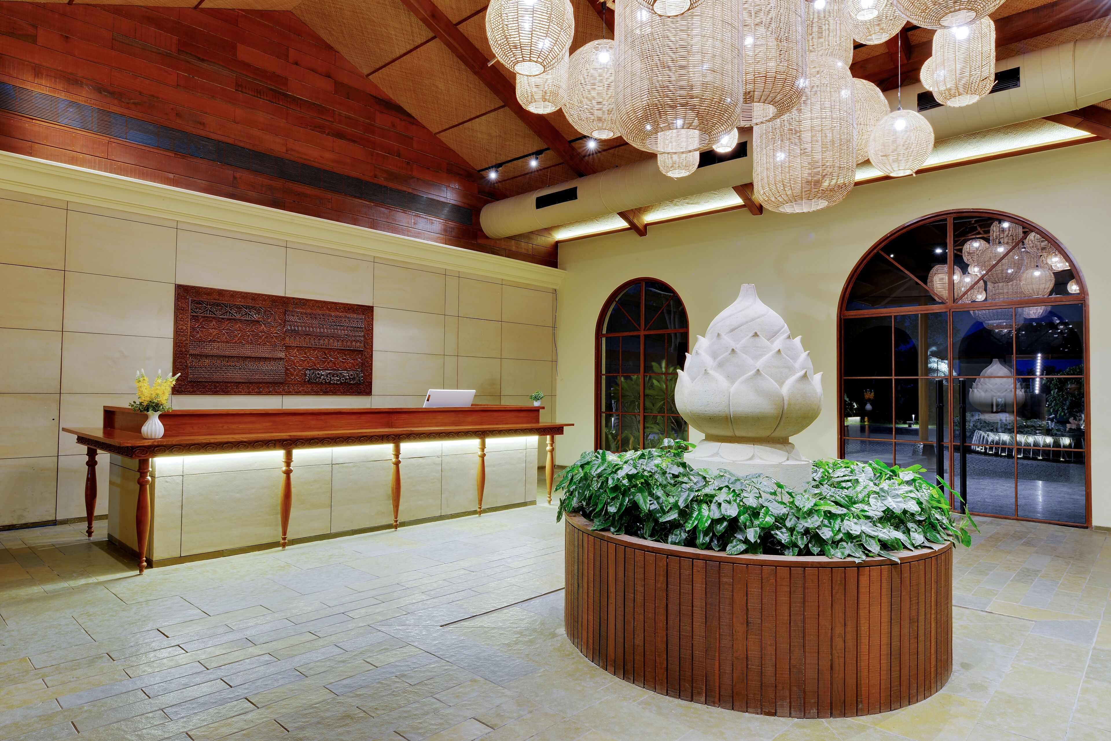 A reception area with a wooden reception desk, a large potted plant, and a decorative wall panel.
