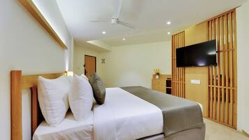 A neatly made bed with pillows, a ceiling fan, a flat-screen TV mounted on a wooden panel, and a wooden wardrobe with a sliding door.