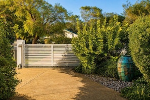 A gated entrance with a concrete pathway, surrounded by lush greenery and a large green barrel.