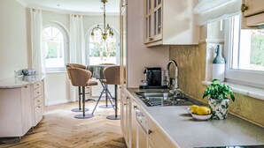 Une cuisine moderne avec un parquet en bois disposé en motif chevron, un îlot central doté d’un évier et un coin repas avec deux chaises.