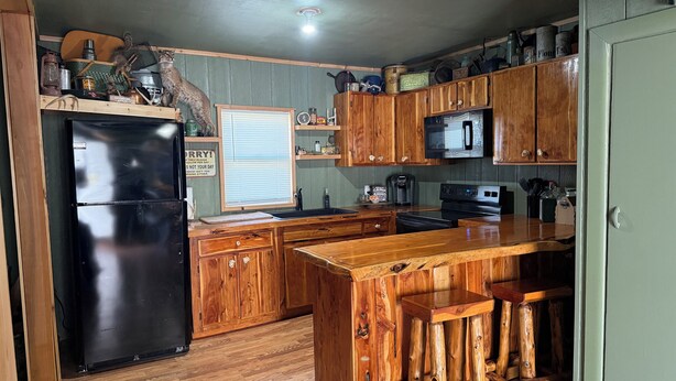 A compact kitchen with wooden cabinets, a black refrigerator, a microwave, and a coffee maker.