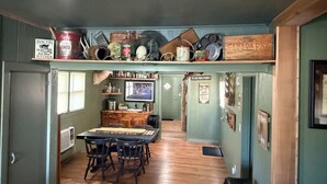 A rustic kitchen with wooden shelves holding various kitchenware and a dining area with a table and chairs.