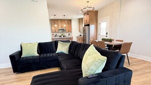 Ein modernes Wohnzimmer mit einem Ecksofa, einem Essbereich und einer Küche im Hintergrund.