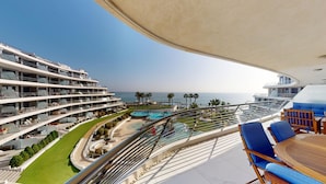 Un balcon avec vue sur une piscine, un hôtel à plusieurs étages et l’océan.