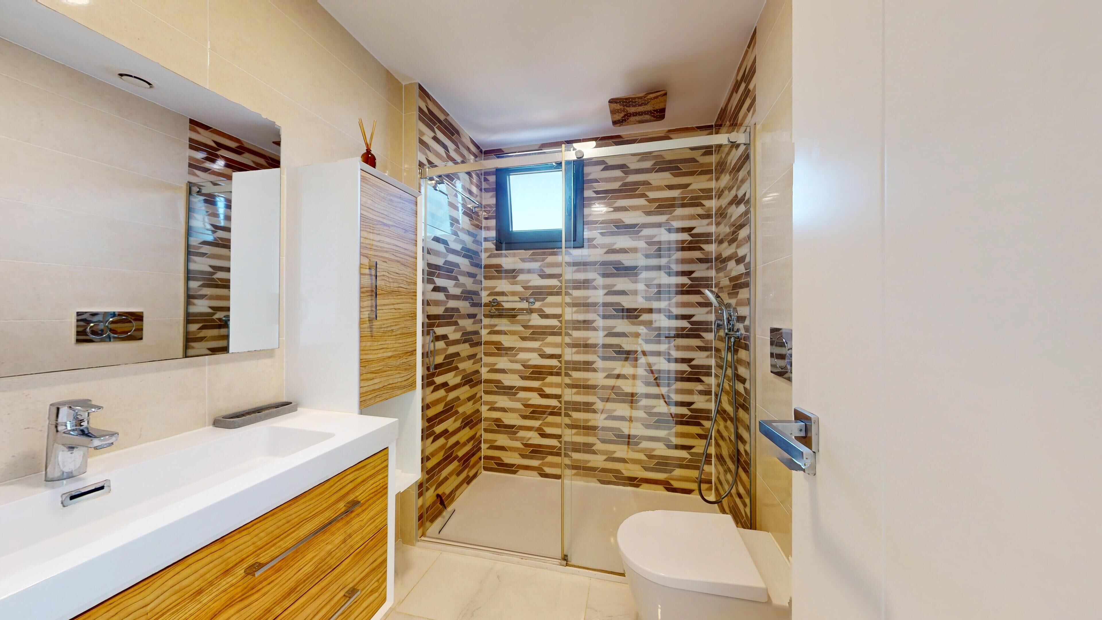 Un baño moderno con ducha de vidrio, tocador de madera y un espejo grande.
