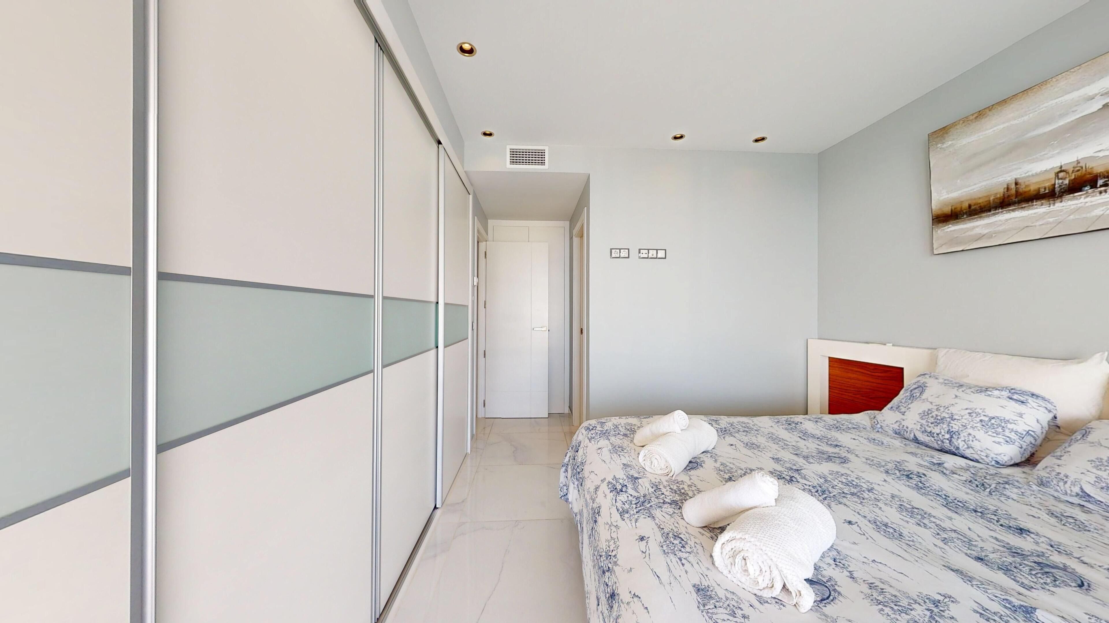 A modern bedroom with a large bed, a glass partition wall, and a cityscape painting on the wall.