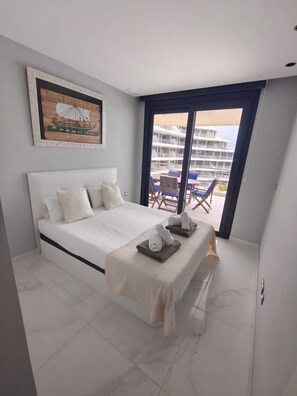 A hotel room with a large bed, a balcony with a view of other buildings, and a painting on the wall.