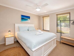 Une chambre à coucher comprenant un lit, une table de chevet, une lampe, un ventilateur de plafond, des œuvres d’art, des fenêtres et un banc.