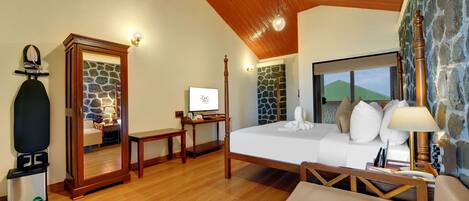 Un dormitorio con techo de madera, pared de piedra, cama con ropa blanca, escritorio con computadora y espejo.