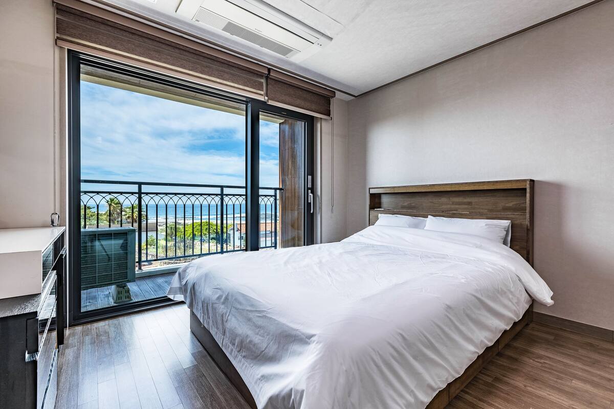 A modern bedroom with a large bed, sliding glass doors to a balcony, and a view of the outdoors.