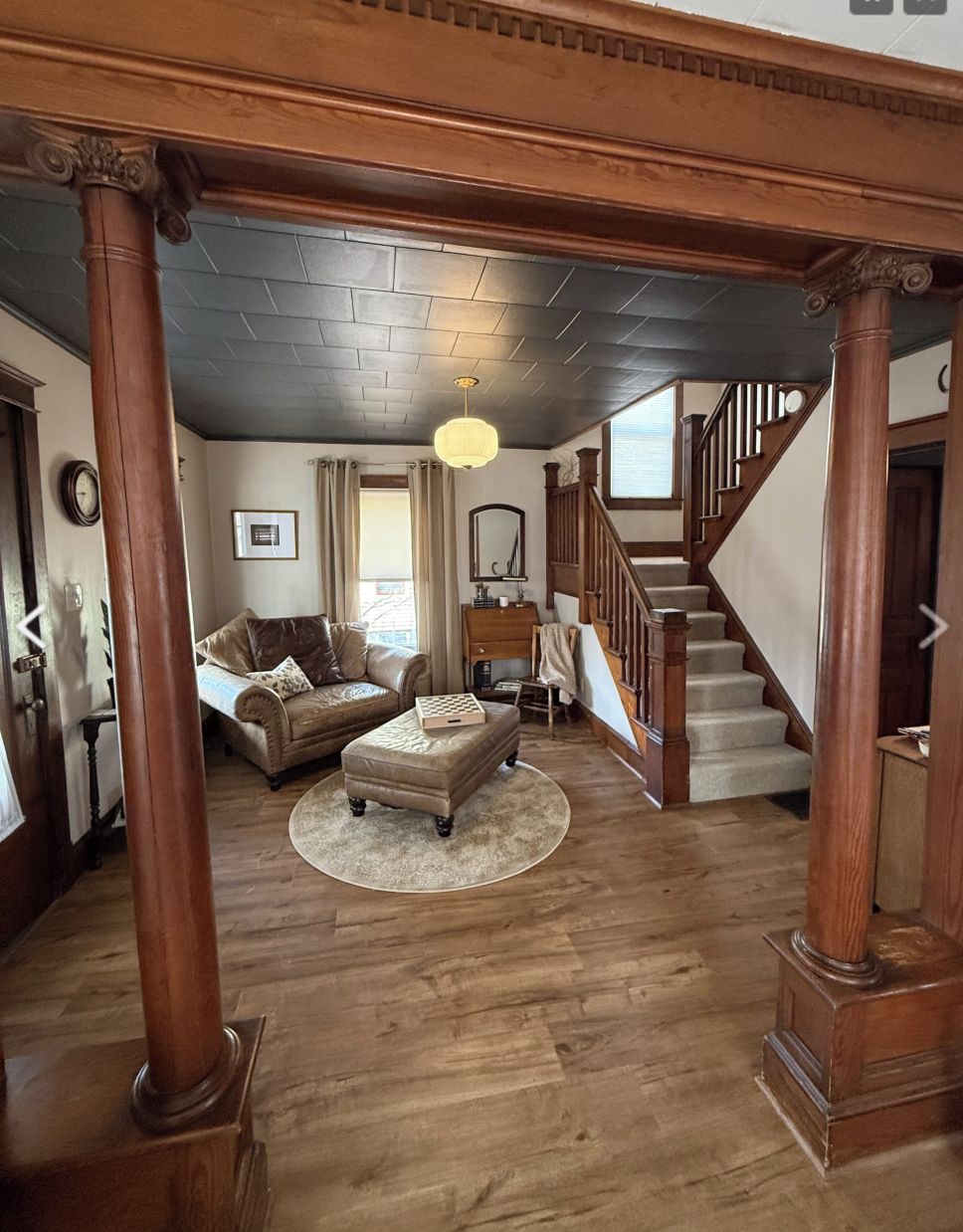 A spacious living room with a wooden staircase, a fireplace, and a large window.