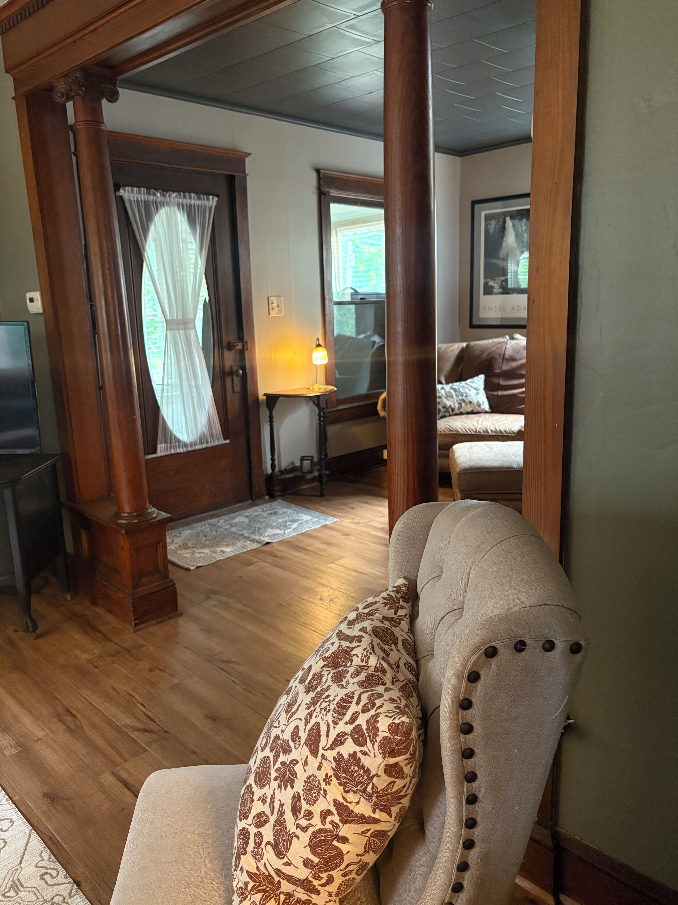 A room with a wooden floor, a chair with a patterned cushion, a lamp, and a window with curtains.