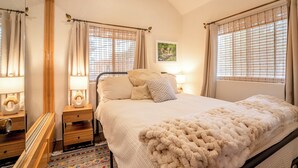Une chambre à coucher avec un grand lit, deux tables de chevet avec des lampes, un miroir et une fenêtre avec des rideaux.