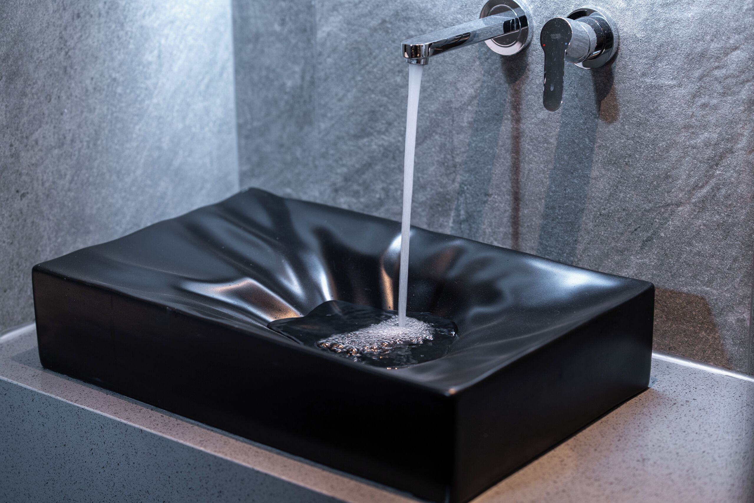 A black rectangular sink with a single faucet against a textured wall.