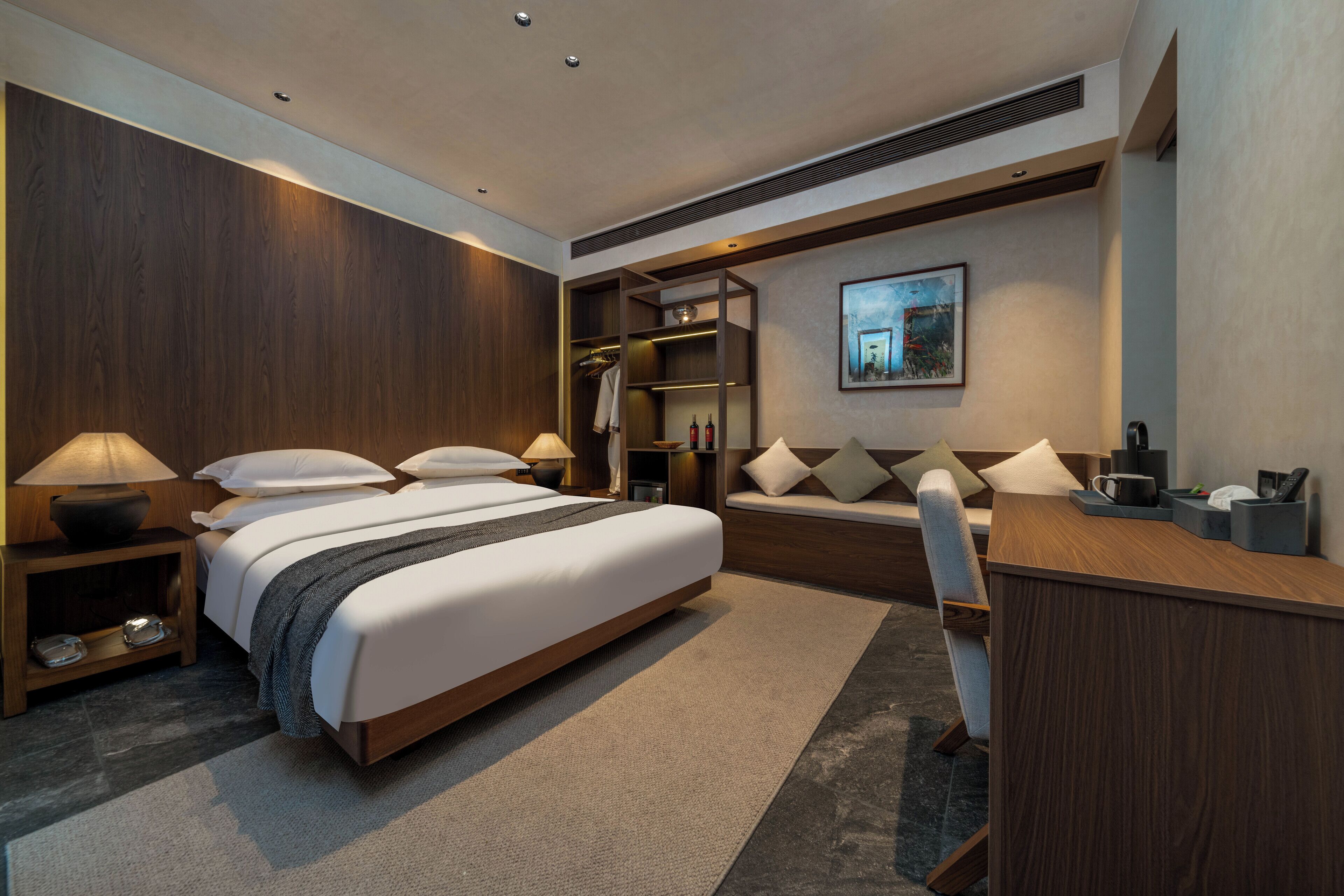 A modern hotel room with a large bed, bedside tables, a desk, and a wardrobe.