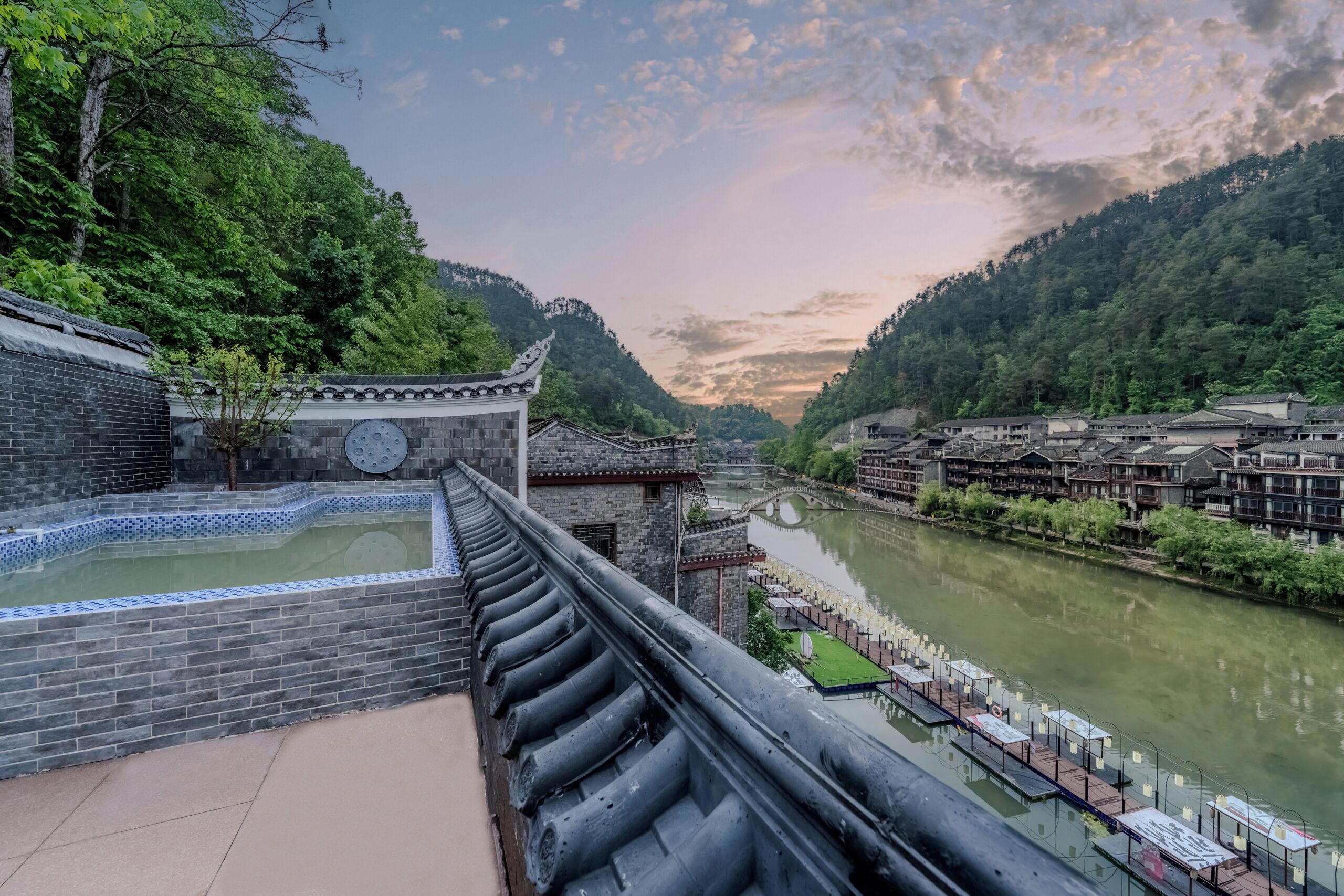 A traditional Chinese courtyard with a tiled pool, wooden buildings, and a river.