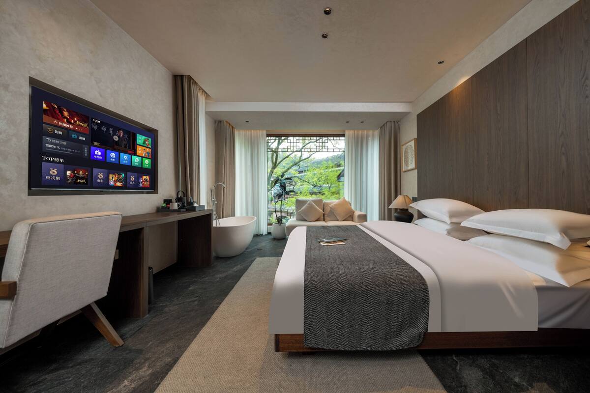 Una habitación de hotel moderna con una cama grande, un escritorio y un televisor montado en la pared.