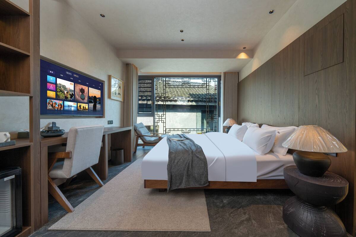 Una habitación de hotel moderna con una cama grande, un escritorio y un televisor mostrando imágenes.