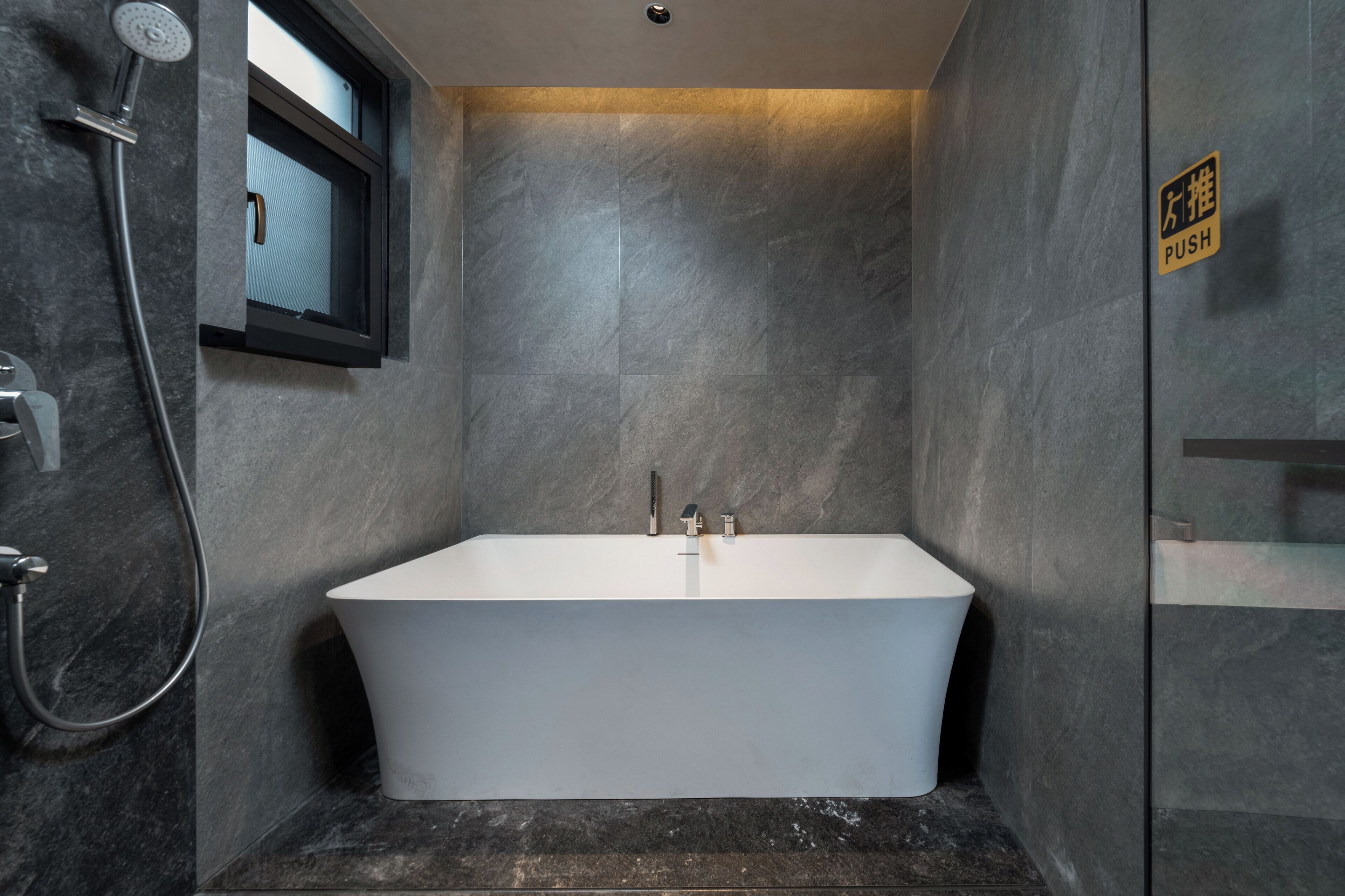 A modern bathroom with a freestanding bathtub, a showerhead, and a window.