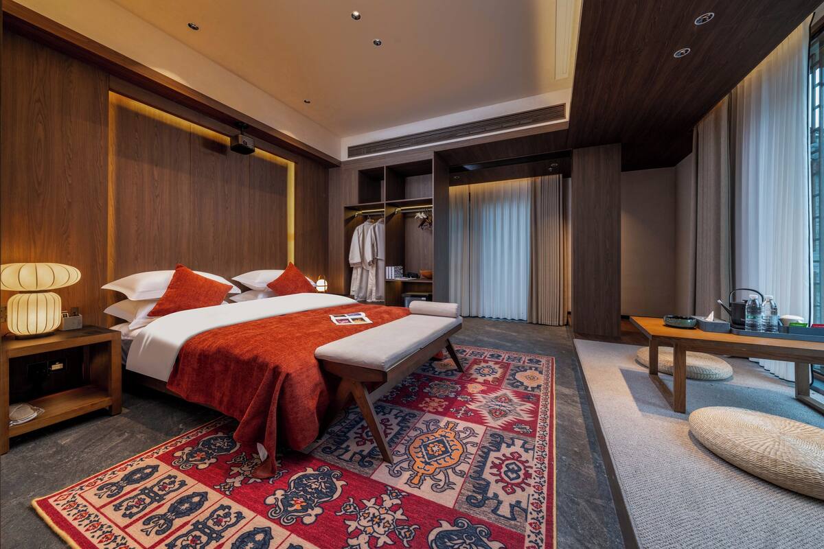Una habitación de hotel moderna con una cama grande, un vestidor, una zona de estar y vistas a la ciudad.