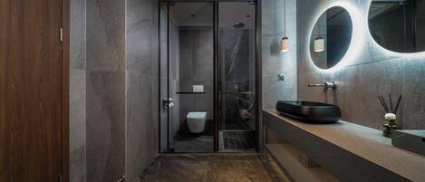 A modern bathroom with a glass shower enclosure, a wooden door, a round mirror, and a black basin.