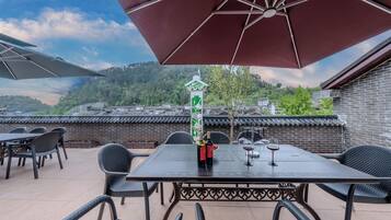 Une terrasse extérieure avec une table dressée pour le repas, entourée de chaises en osier, sous un grand parasol.