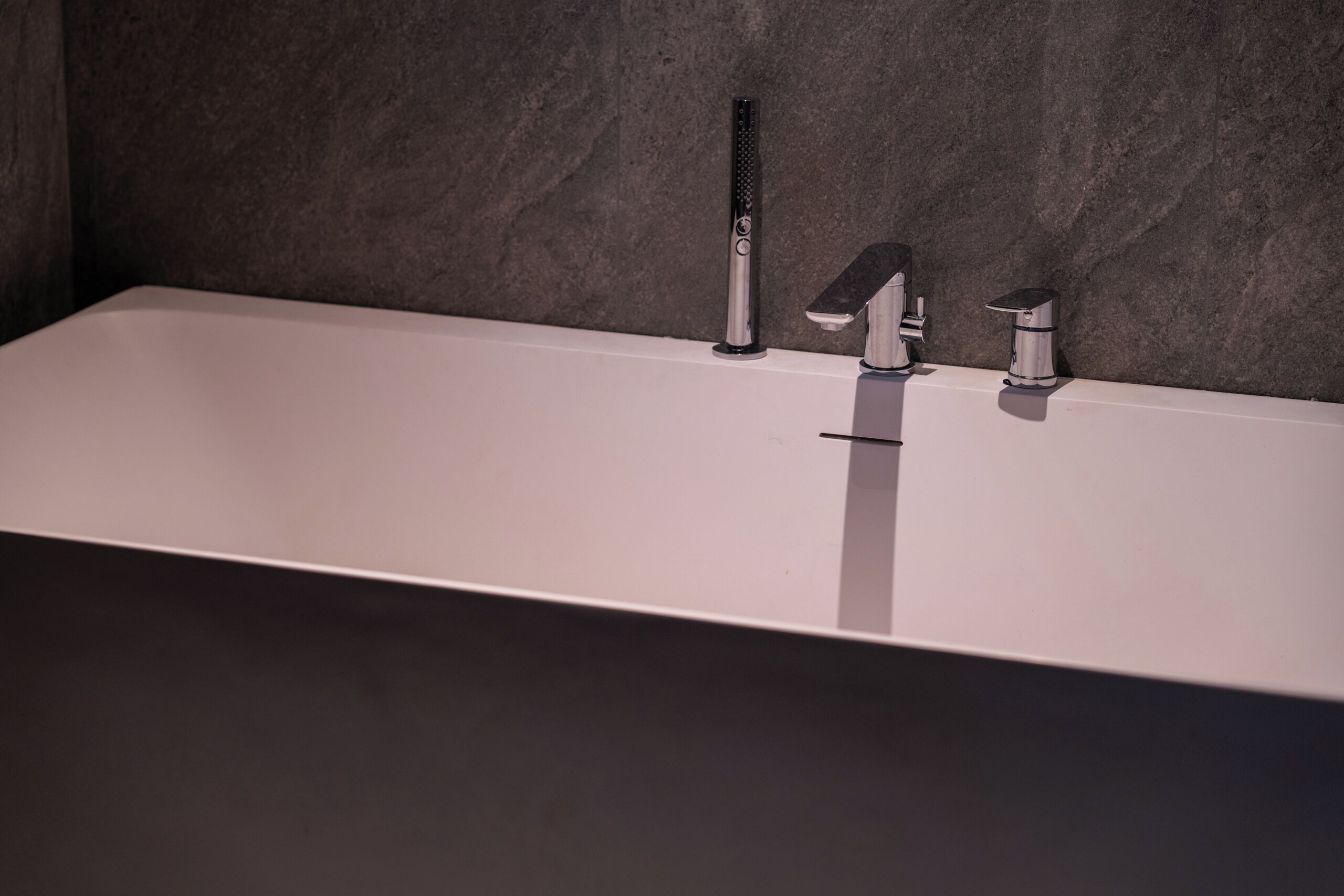 Un baño moderno con una bañera rectangular, un solo grifo y un cabezal de ducha de mano.