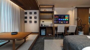 Habitació d'hotel moderna amb escriptori de fusta, llit amb estovatge estampat, petita prestatgeria amb objectes i pantalla digital que mostra contingut.