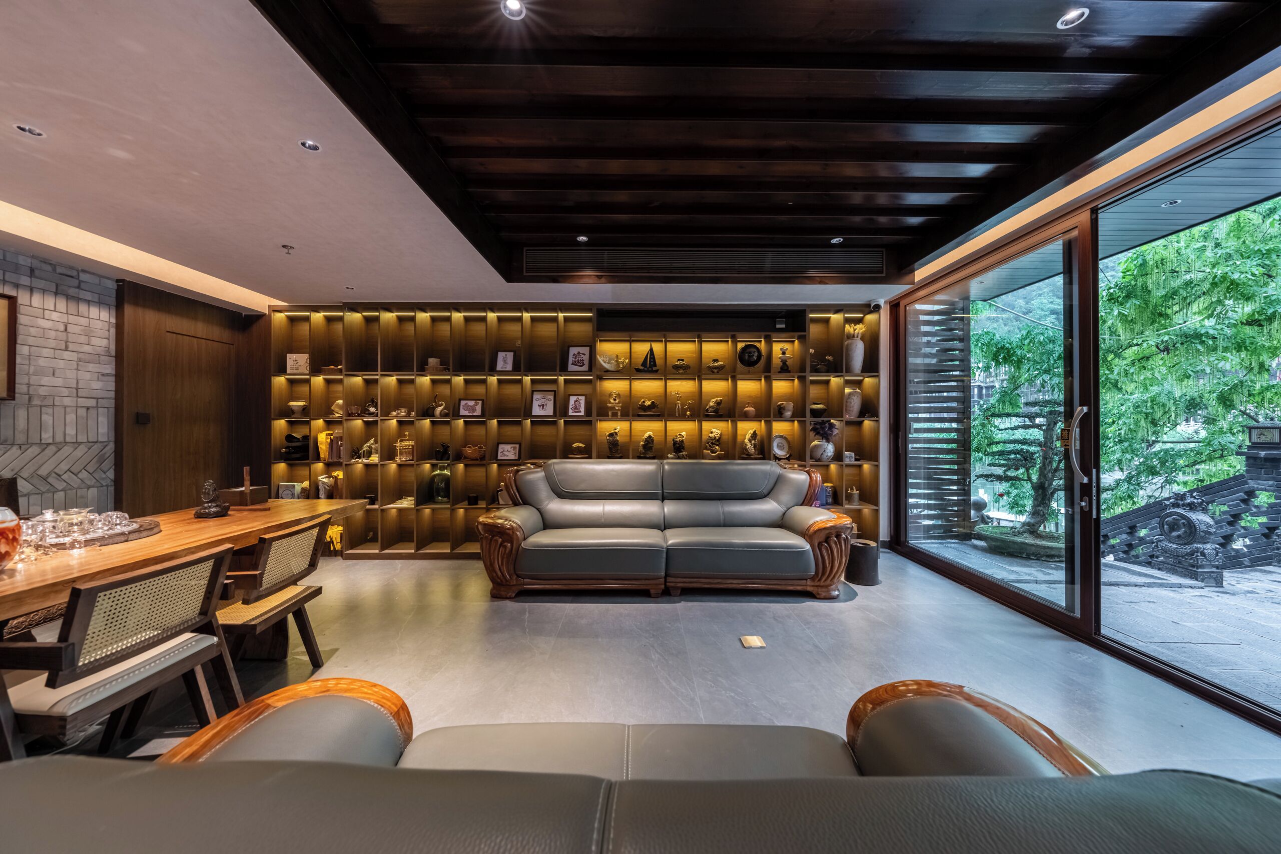 A modern living room with a wooden dining table, leather sofa, and a wall of illuminated shelves.