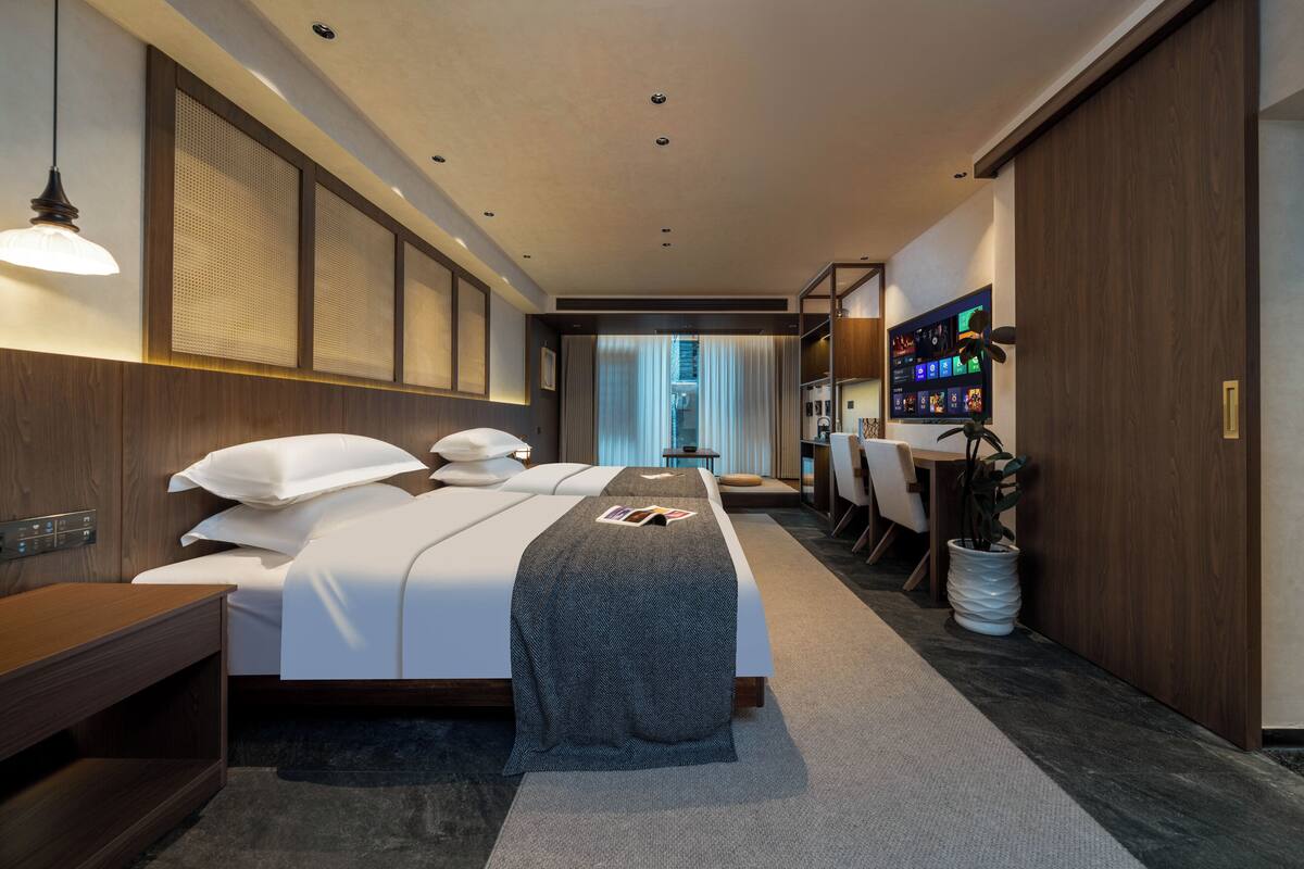 Una habitación de hotel con cama, mesita de noche, lámpara y televisor en la pared.