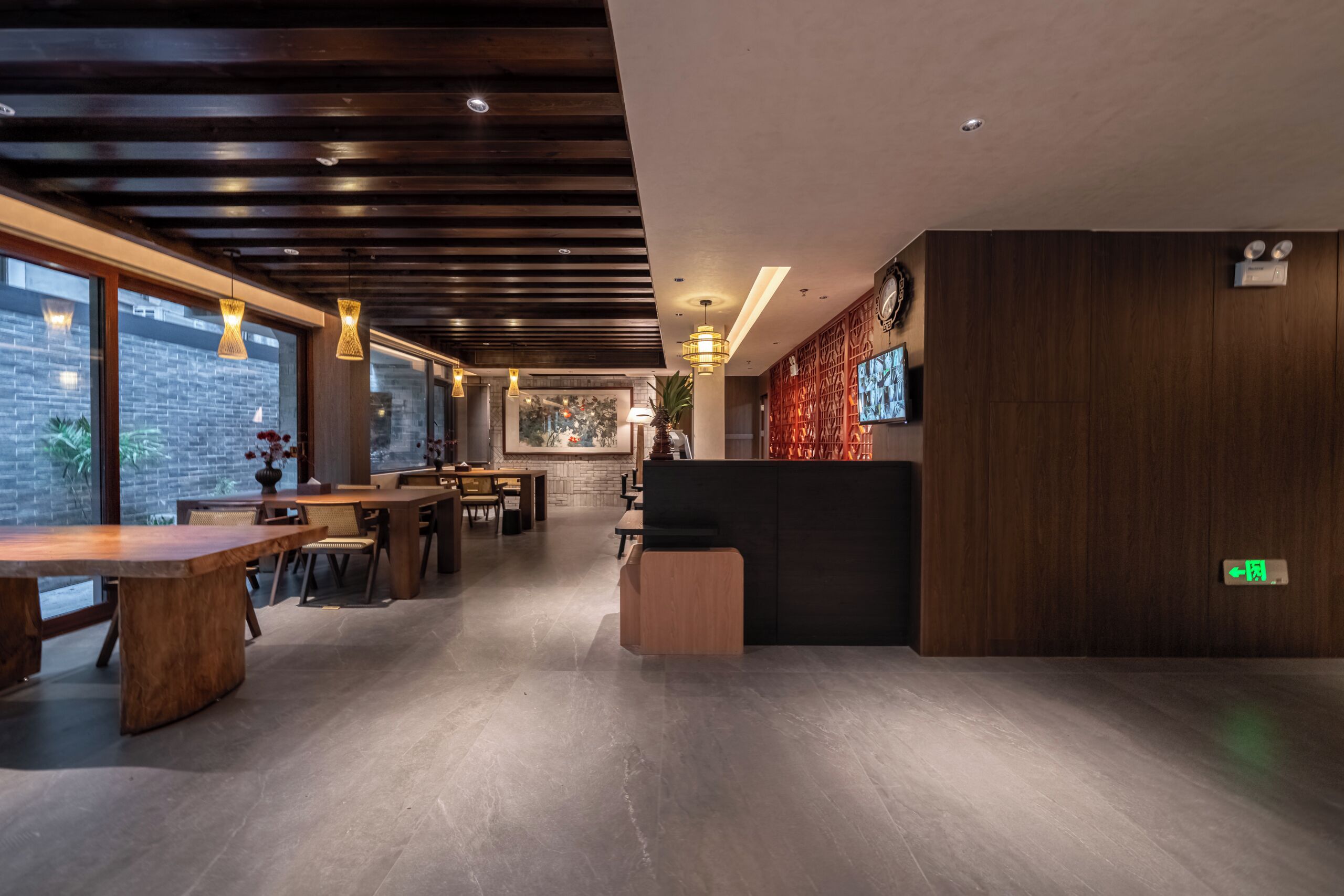 A modern interior with wooden tables and chairs, a reception desk, and a large TV screen on the wall.