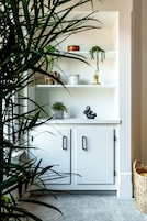 A white cabinet with shelves, a basket, and a potted plant.