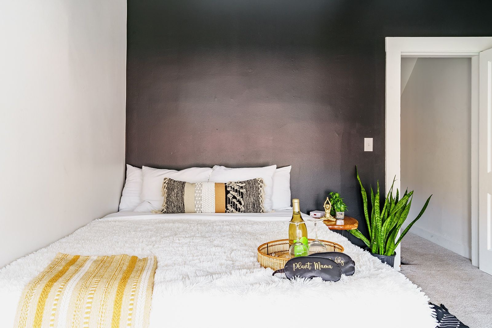 A bedroom with a bed, a bedside table, a potted plant, and a decorative item on the floor.