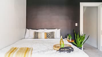 A bedroom with a bed, a bedside table, a potted plant, and a decorative item on the floor.