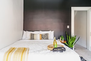 A bedroom with a bed, a bedside table, a potted plant, and a decorative item on the floor.