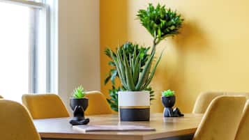 Une table à manger avec des chaises, des plantes en pot et une fenêtre avec des stores.
