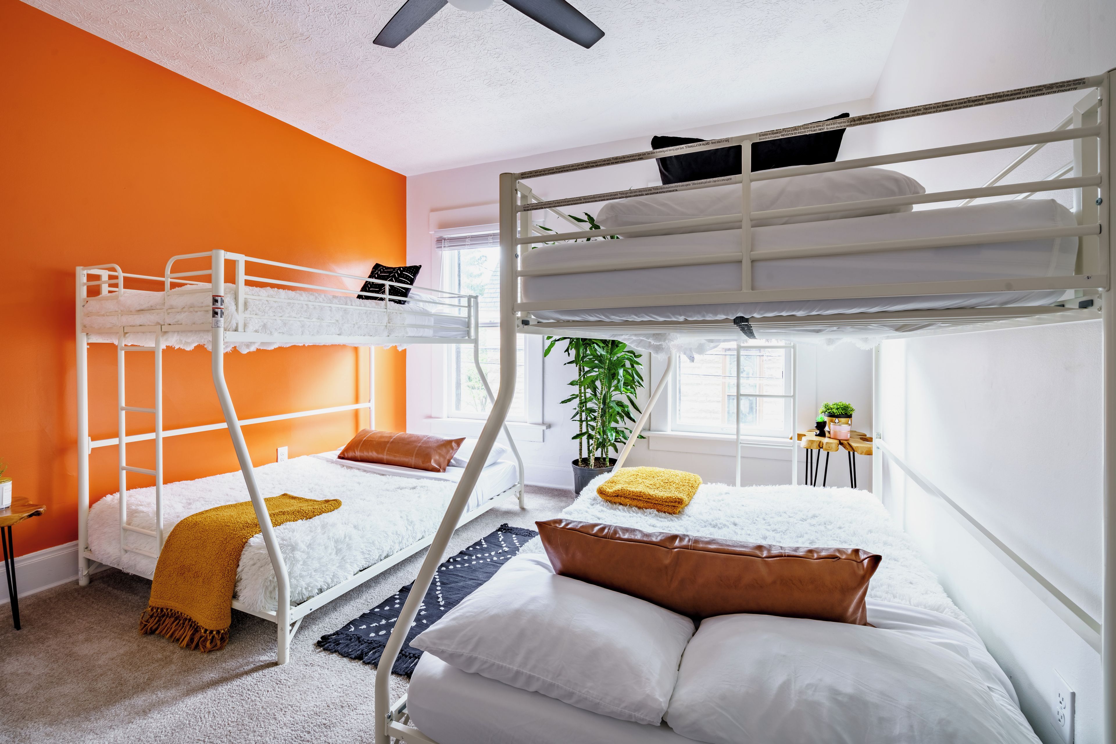 Ein Schlafzimmer mit Etagenbetten, einem weißen Deckenventilator, einem Fenster mit Jalousien, einem Blumentopf und einem kleinen Tisch mit Pflanze.