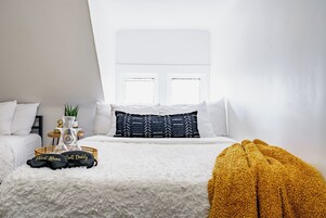 Ein Schlafzimmer mit einem Bett, Kissen, einem Nachttisch mit Pflanze und einem Fenster.